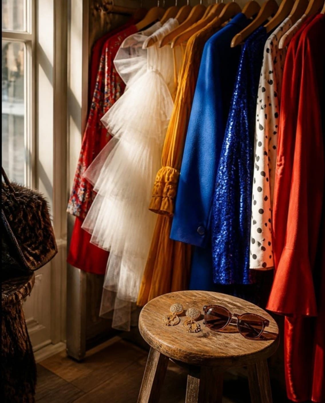 A wardrobe rail with red, cobalt and white garments in afternoon light